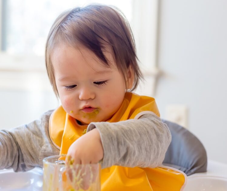 Baby in orange bib eating puree food