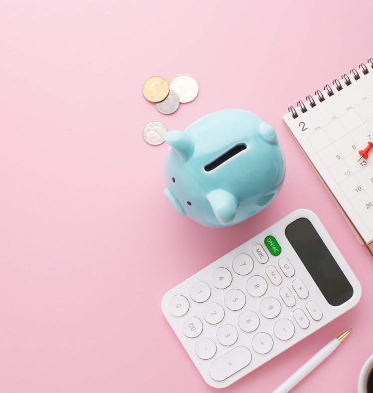 A piggy bank, calculator and a calendar sitting on a pink desk