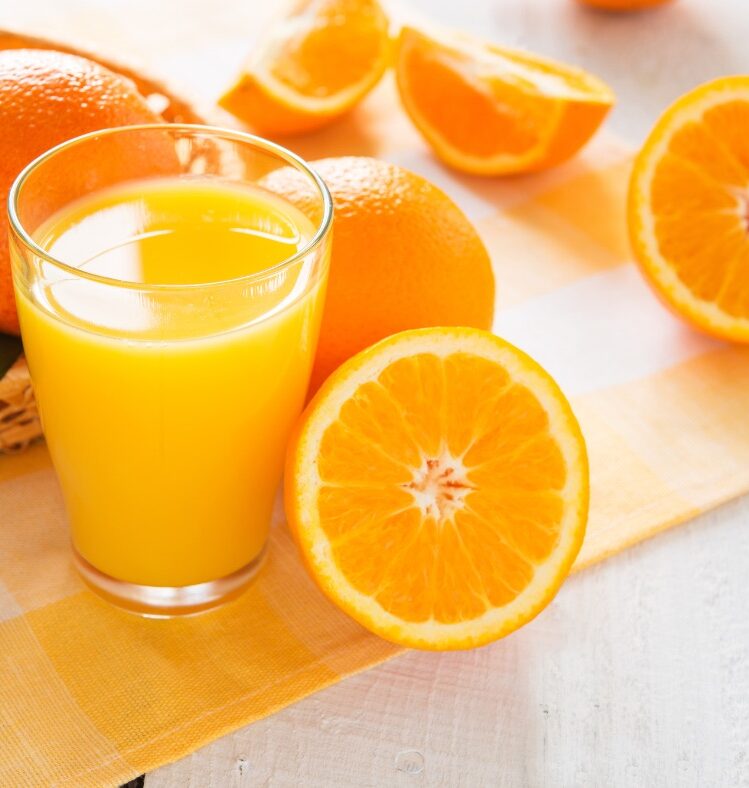 Sliced oranges sitting next to a glass of orange juice