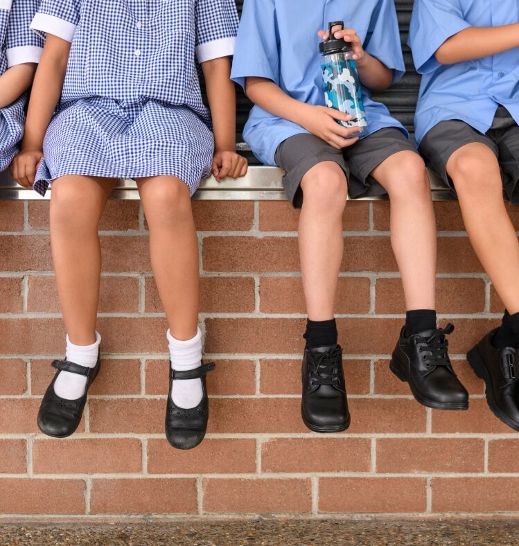 Four school children sitting on a brick wall