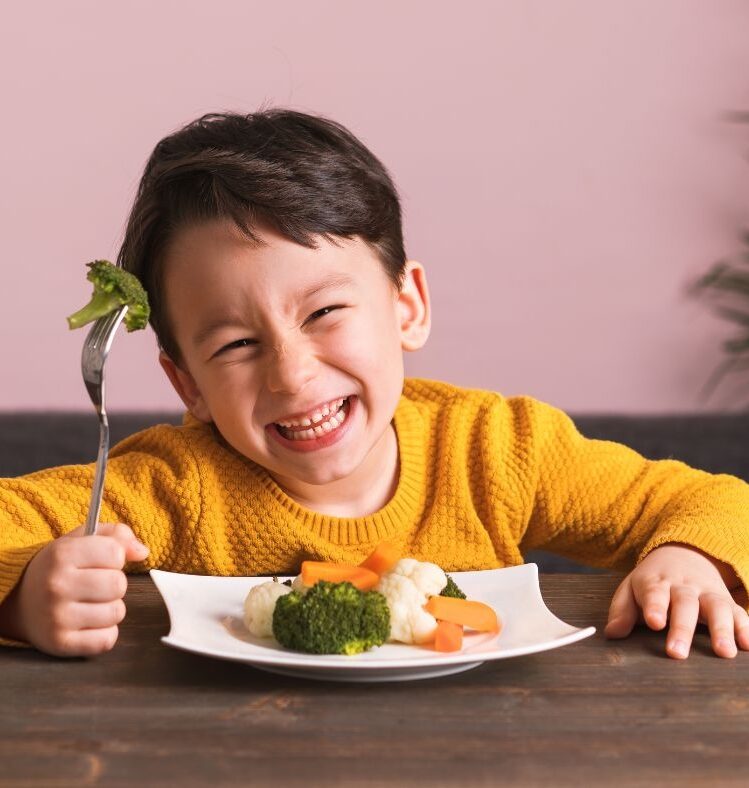 Smiling child at a table eating from a plate of vegetables