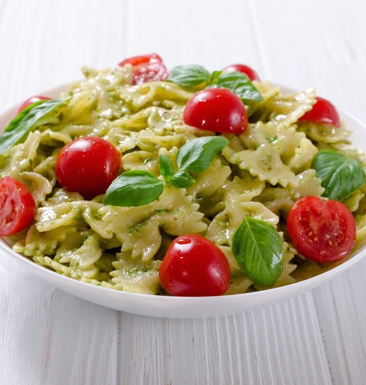 Pesto pasta salad in a white bowl with tomatoes and basil