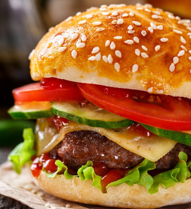 A beef burger with grilled onion mustard and tomato between a sesame bun