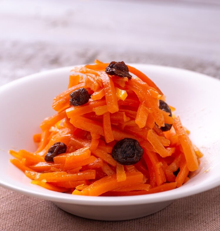 Shredded carrot and raisins in a white bowl