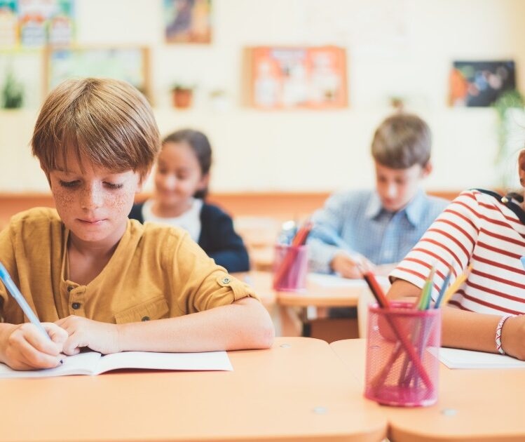 Children writing in notebooks at their desks in a classroom